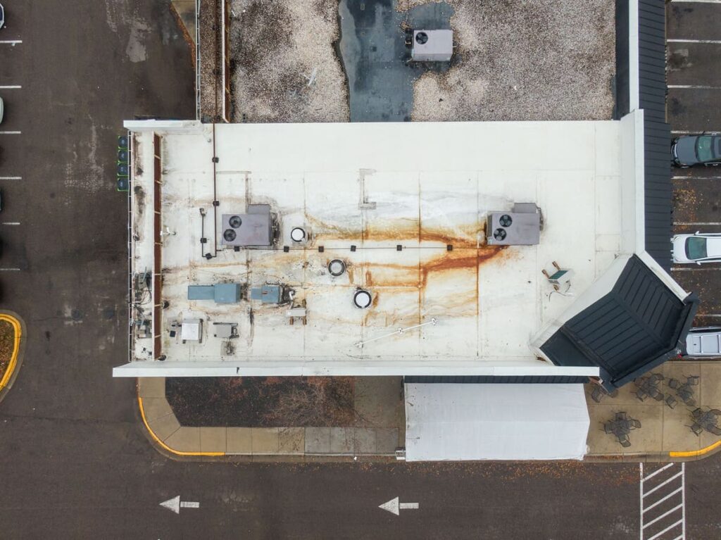Aerial view of a commercial flat roof with visible rust stains and water damage, showcasing the need for professional roof leak repair services.