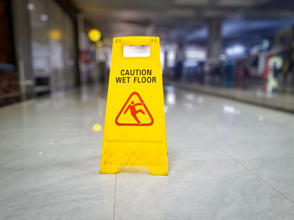 Yellow caution wet floor sign on a shiny indoor floor, emphasizing the potential hazards of roof leaks in commercial spaces.